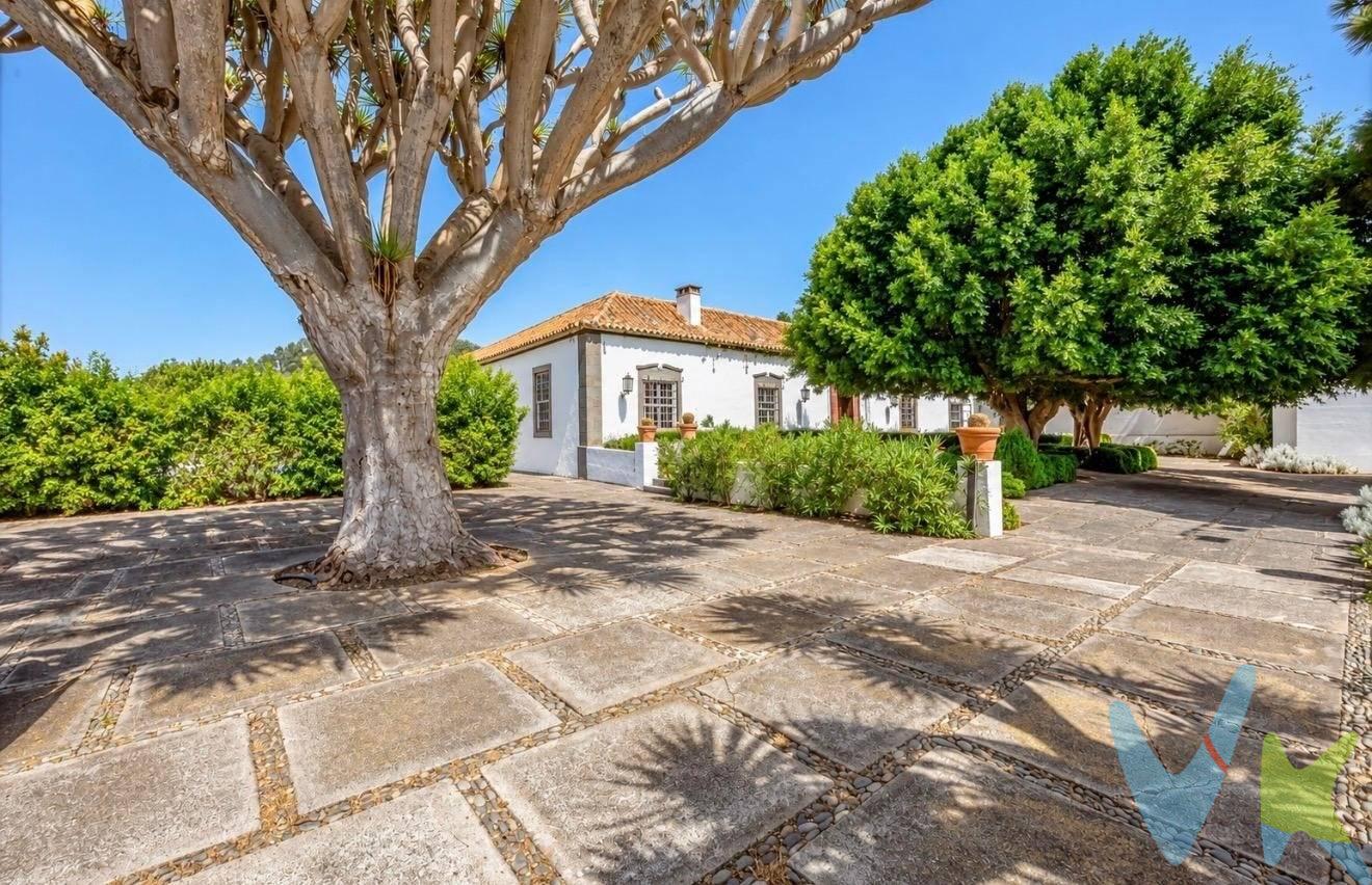 Sobre una parcela de 3.055 m², esta propiedad cuenta con 1.651 m² de superficie construida. Su arquitectura se articula en torno a un amplio patio canario, que aporta luz natural y conecta las distintas estancias de la vivienda. Un gran portalón de madera enmarcado en piedra da acceso al hall principal. A su derecha se abre un luminoso salón con techos de aproximadamente cuatro metros de altura. A continuación, un segundo salón de generosas dimensiones, también con techos altos, incorpora una gran chimenea de piedra y ofrece un espacio acogedor para la vida diaria. La zona de día continúa con un comedor u office provisto de un altillo destinado a almacenaje. Una vidriera de estilo inglés lo separa de la amplia cocina, que dispone de despensa y cuarto de lavandería. Desde la cocina se accede directamente al exterior a través de una puerta lateral, junto a una zona cubierta de apoyo y almacenamiento. Una galería abierta al patio canario comunica con el aseo de cortesía y distribuye las diferentes áreas de descanso. Desde ella, una escalera conduce a la planta superior, donde se encuentran dos dormitorios, dos baños y una zona de lencería. En la planta principal se ubican otros tres dormitorios de buenas dimensiones, con posibilidad de configurarse como dobles, que comparten un amplio baño. La suite principal ocupa un sector diferenciado de la vivienda. Está formada por un espacioso dormitorio, un baño de grandes dimensiones y una estancia comunicada destinada a vestidor y despacho. Sus estanterías de madera aportan carácter y calidez a este espacio, que vuelve a conectar con el hall y completa el recorrido alrededor del patio interior. En el exterior, la propiedad ofrece una amplia zona de aparcamiento y un camino que bordea la vivienda. El jardín dispone de un agradable espacio destinado a comidas y reuniones al aire libre. En la parte posterior de la propiedad se encuentran tres apartamentos independientes, actualmente alquilados, que aportan un atractivo componente de inversión y permiten combinar el uso residencial de la vivienda principal con la obtención de rentas adicionales. El recorrido exterior se completa con una cancha multideportiva y varias dependencias auxiliares destinadas al almacenamiento de material de jardinería y otros enseres. Una propiedad singular por la amplitud de sus espacios, el carácter de su arquitectura, la presencia constante del patio canario y la versatilidad que ofrece la combinación de una gran vivienda principal con tres unidades independientes. 